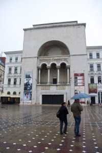Front of opera house with two people standing outside holding an umbrella