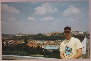 Prof. Berglund in a t-shirt and baseball cap posing in front of the Prague skyline on a summer day