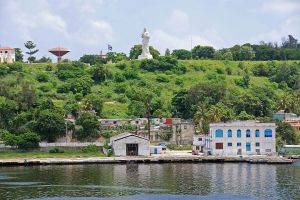 A 20m tall statue of Christ on a green hill, overlooking low buildings along the bay
