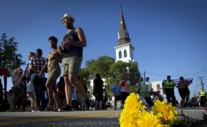People walk past a bunch of flowers left in memorial on the ground as they take part in a "Black Lives Matter" march past Emanuel AME Church on June 20, 2015