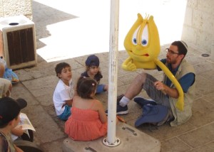 Man holding a large anthropomorphic harp puppet teaches a group of small children.